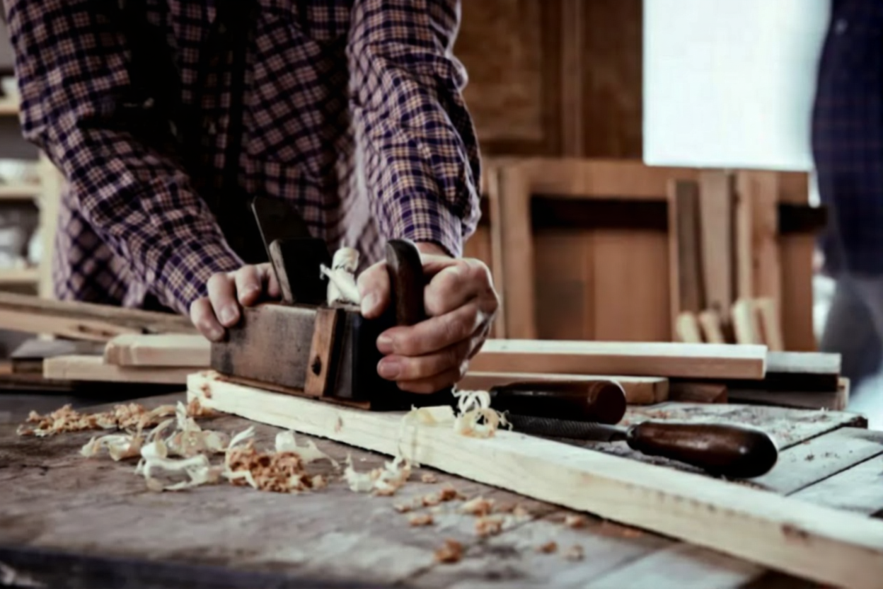 Carpenter or joiner planing a plank of wood smoothing the surface in a close up view on his hands and the tool on a workbench.